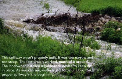 This spillway wasn't properly built. It was too narrow and too steep. The first time it worked, much of it eroded. The landowner installed a gable-rock device to keep dirt in place. As you can see, water is still forceful. Build the proper spillway in the beginning.